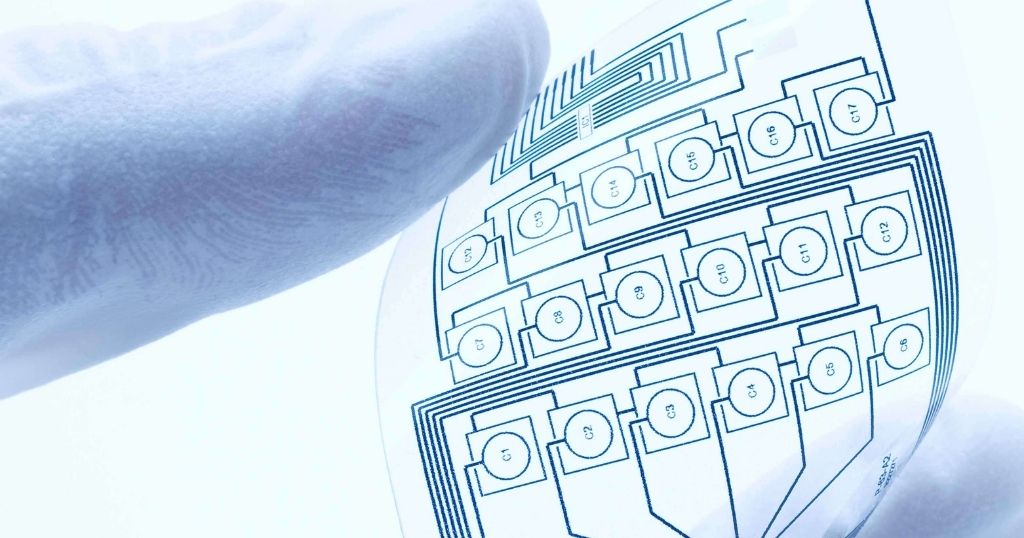 Close up image of someone holding a transparent sheet with printed electronics on it